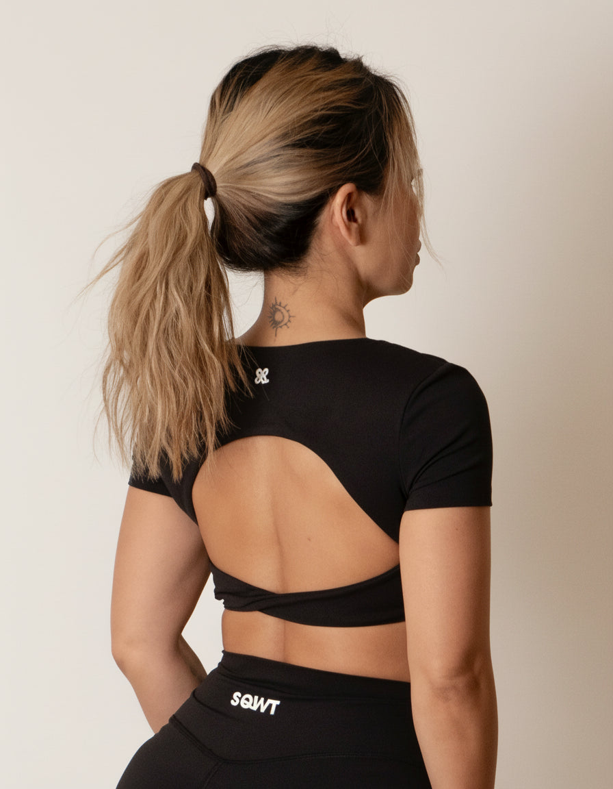 Black short-sleeve crop top/bra top with a twisted knot front and back, open cut-out back, and a deep V-neckline. Ideal for women's activewear, gym, and yoga.