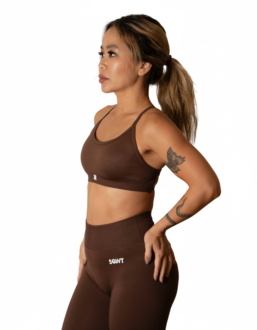 Dark brown sports bra with thin straps, featuring a cross-back design and supportive front fit, shown on a model from both front and back.
