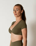 Olive green short-sleeve crop top/bra top with a twisted knot front and back, open cut-out back, and a deep V-neckline. Ideal for women's activewear, gym, and yoga.