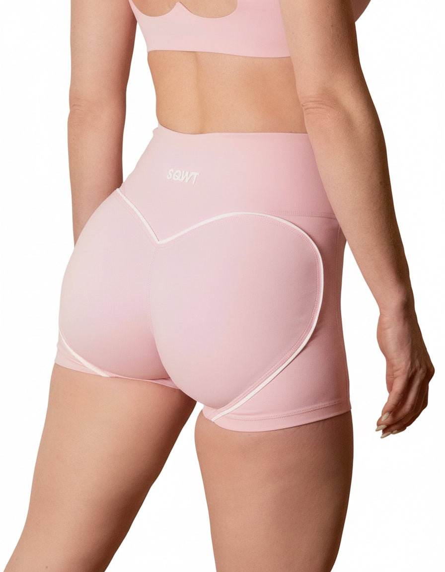 Seamless high-waisted gym shorts in baby pink, featuring a wide V-shaped back waistband with white contrast piping/seaming that enhances the booty shape.
