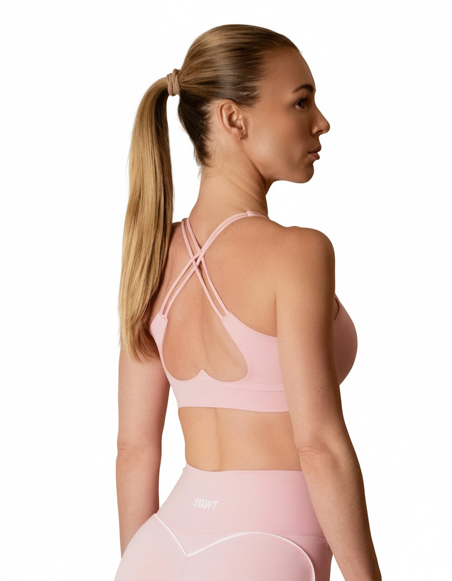 Baby pink light-impact sports bra with a classic scoop neck front and a striking back design featuring criss-cross straps and a large heart-shaped cutout.