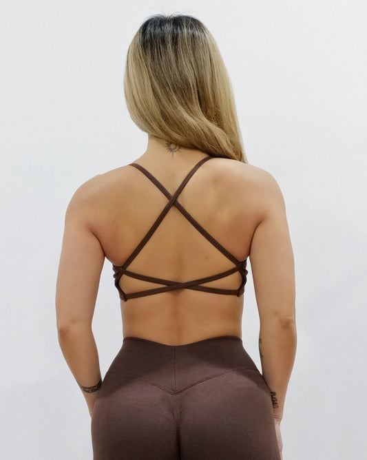 Dark brown sports bra with thin straps, featuring a cross-back design and supportive front fit, shown on a model from both front and back.