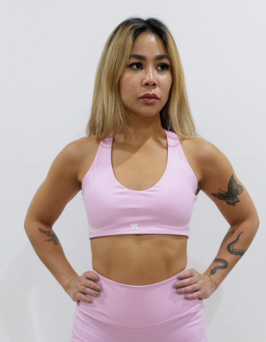 Baby pink light-impact sports bra with a classic scoop neck front and a striking back design featuring criss-cross straps and a large heart-shaped cutout.
