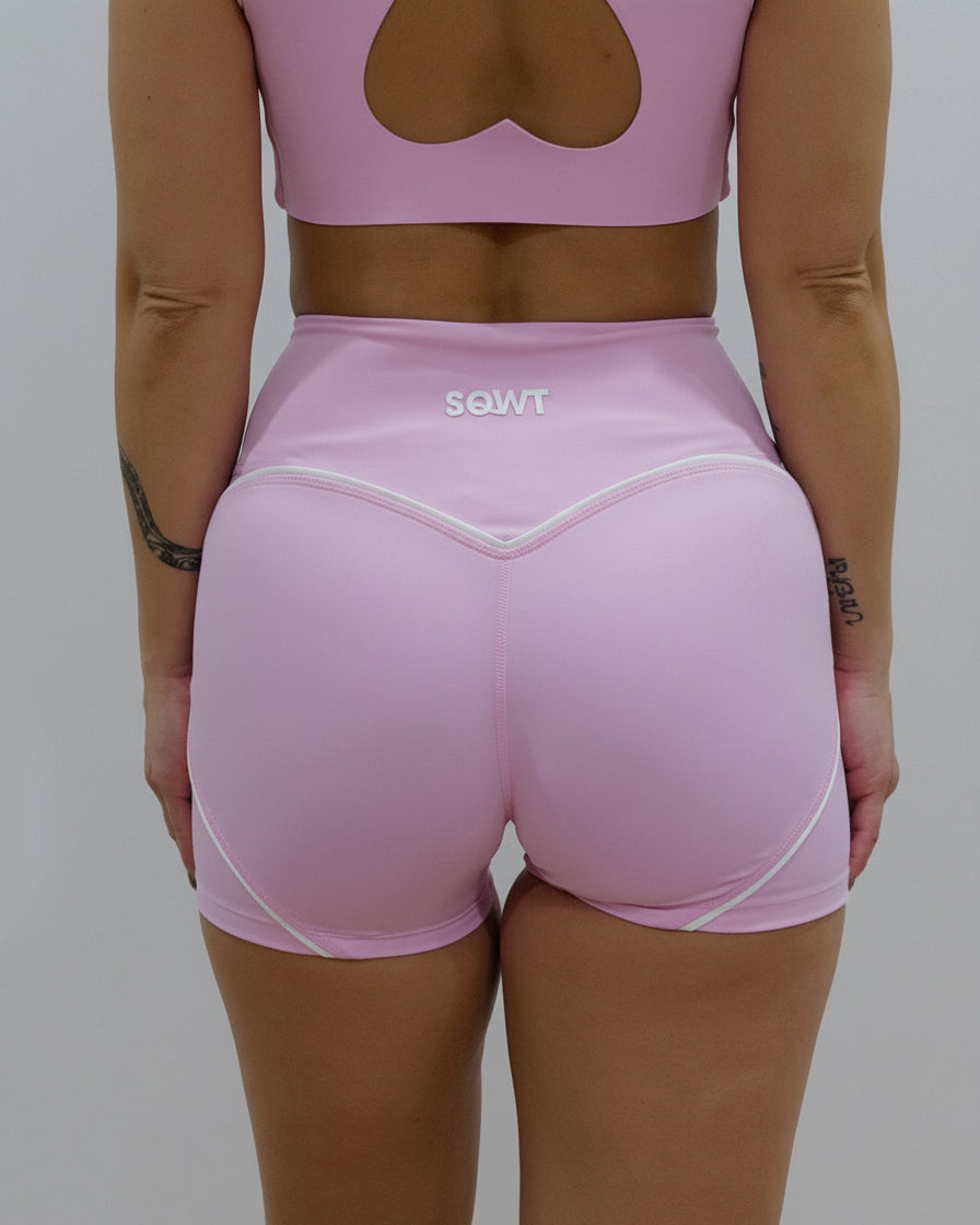 Seamless high-waisted gym shorts in baby pink, featuring a wide V-shaped back waistband with white contrast piping/seaming that enhances the booty shape.