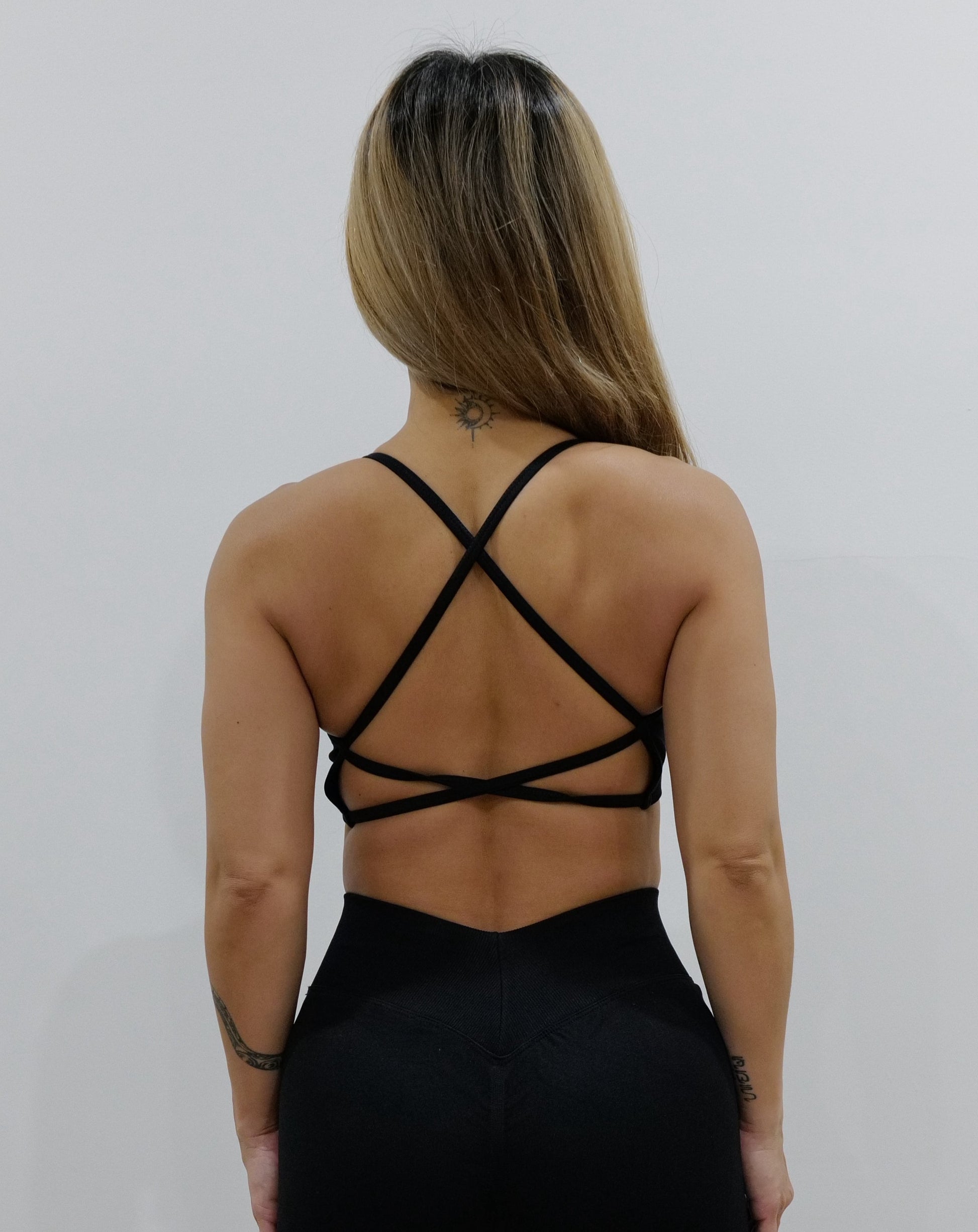 Black sports bra with thin straps, featuring a cross-back design and supportive front fit, shown on a model from both front and back.